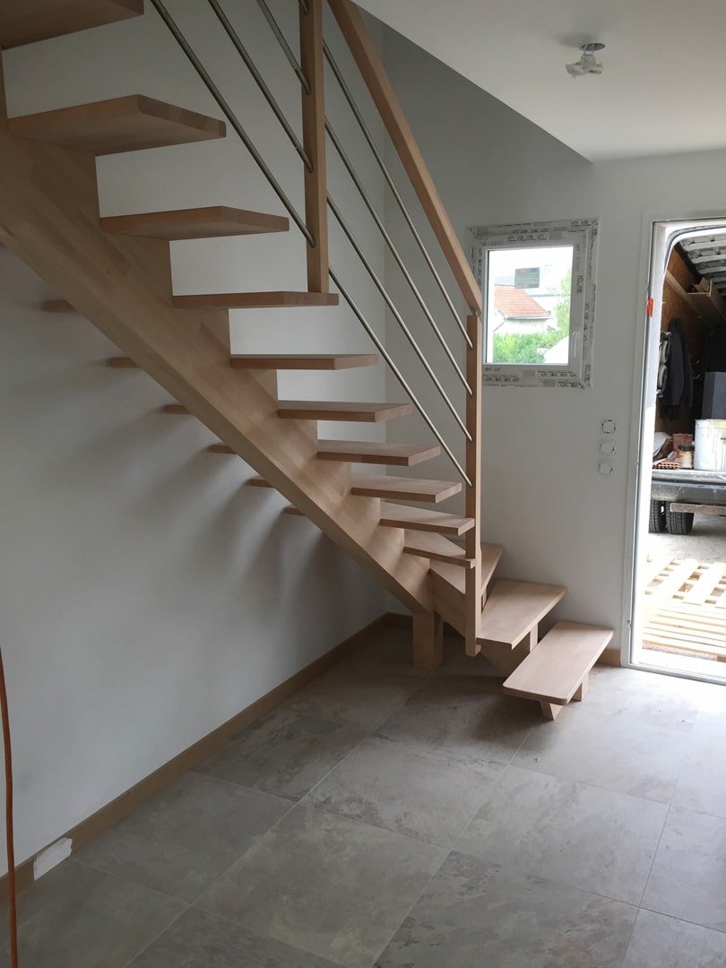 Escalier en bois élégant avec marches en porte-à-faux et garde-corps en câble métallique dans une maison lumineuse.