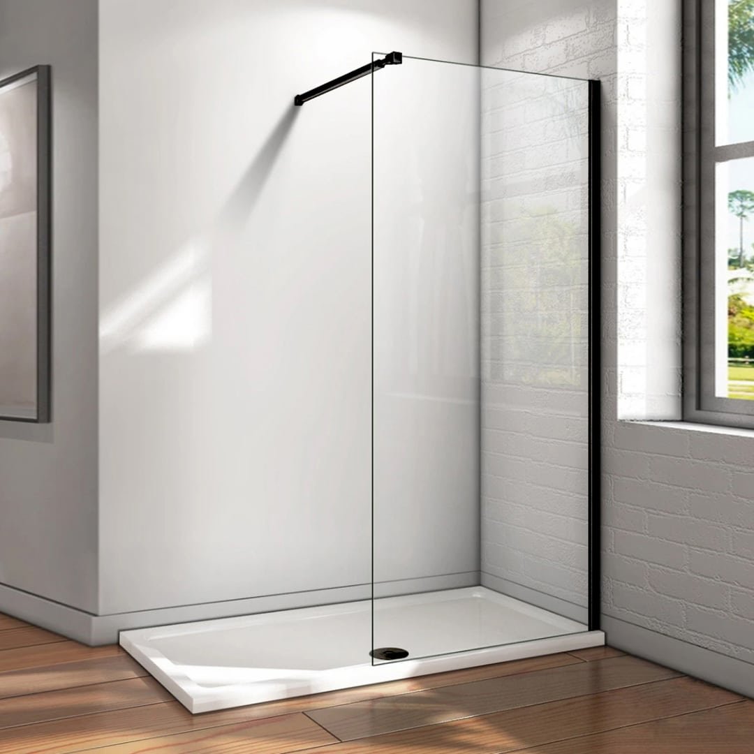 Douche minimaliste avec un seul panneau de verre fixe maintenu par une barre noire, installée dans un coin avec des murs en briques blanches et un s