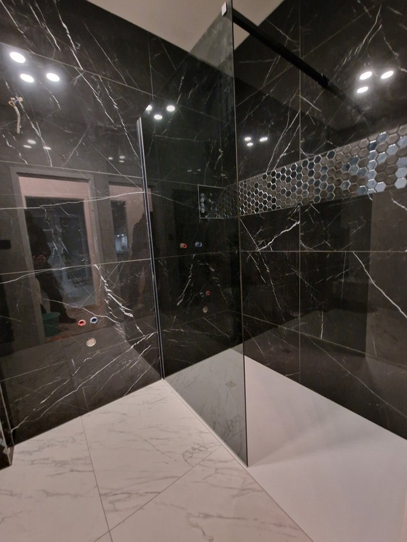 Intérieur d'une salle de bain moderne avec des murs et une douche en marbre noir veiné, des spots encastrés au plafond et un sol en carre