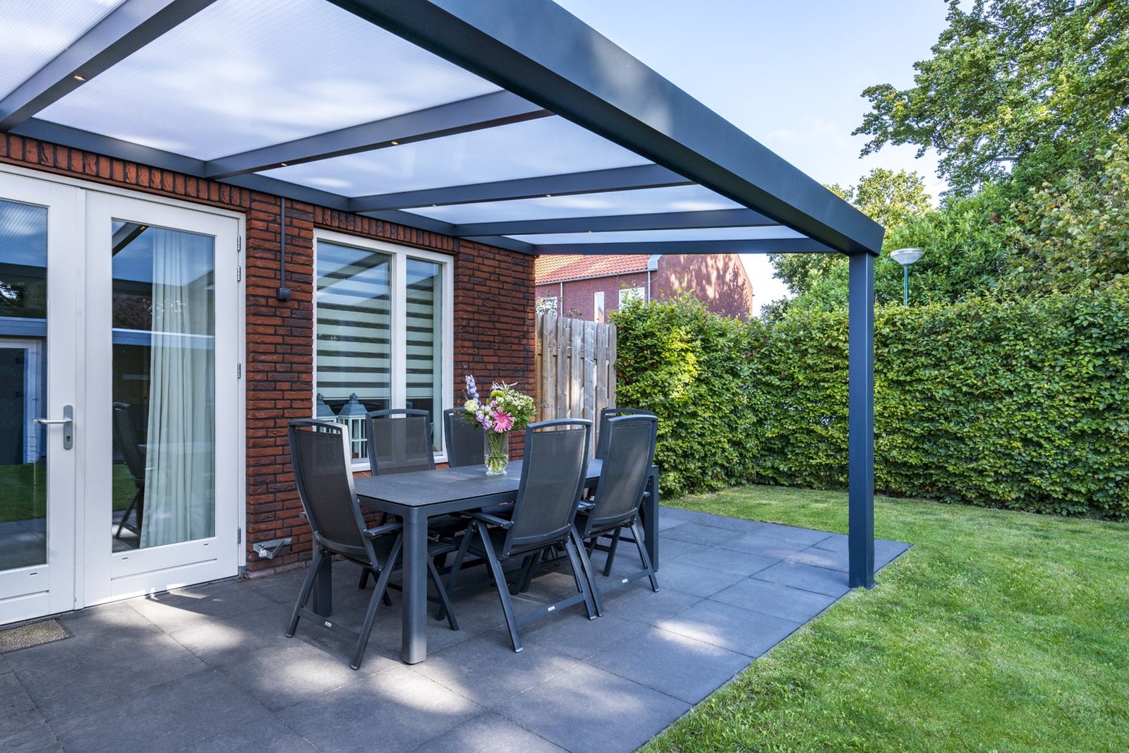 Pergolas Luxembourg élégante avec toiture en polycarbonate, encadrant un espace de repas extérieur avec vue sur le jardin.