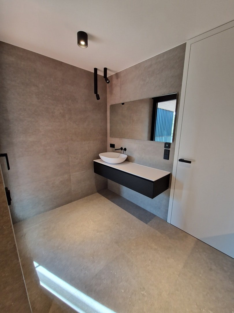 Salle de bain contemporaine avec lavabo suspendu, miroir intégré, éclairage moderne et carrelage effet béton.
