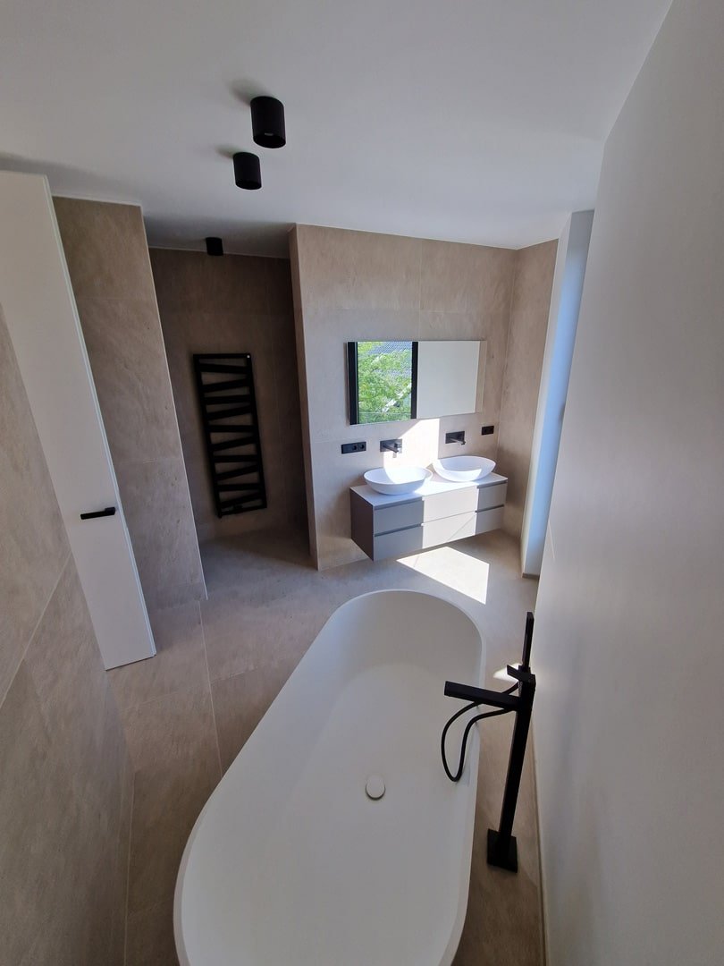 Salle de bain lumineuse avec baignoire îlot, lavabo double suspendu, grand miroir, éclairage encastré et vue sur l'extérieur.
